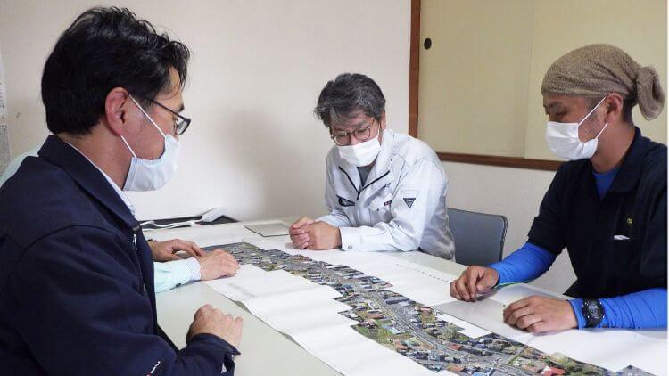 国土交通省　I現場の図面を見ながらインタビューに答える江藤工事次長（右奥）と堀内さん（右手前）CT施工の普及拡大に向けて取組