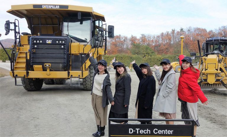 D-teckセンターのICT建機を背景にポーズ